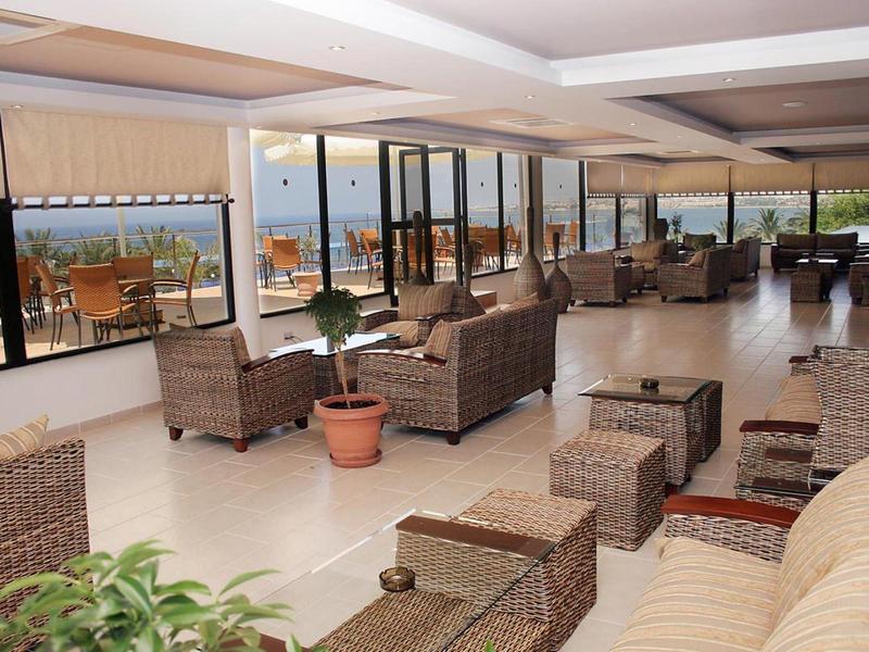 Großer, hell beleuchteter Wintergarten mit Rattanmöbeln und Pflanzen, Blick auf Terrasse und Meer.