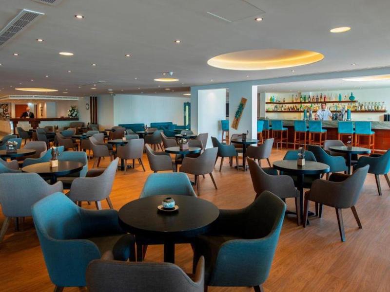 Moderner Bar- und Loungebereich mit runden Tischen, blauen und grauen Sesseln, hellem Holzboden.