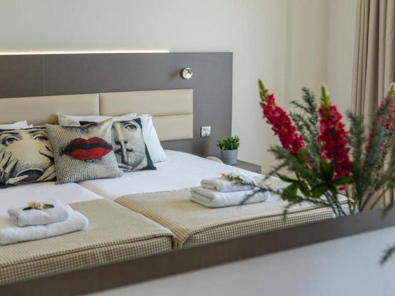 Modernes Schlafzimmer mit Doppelbett, beigen Kissen und frischen roten Blumen im Vordergrund.