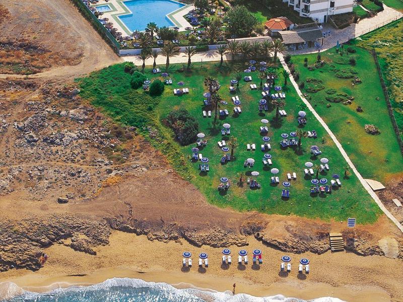 Großes Hotel mit Pool, angrenzender Wiese mit Sonnenschirmen und direktem Zugang zum Strand.