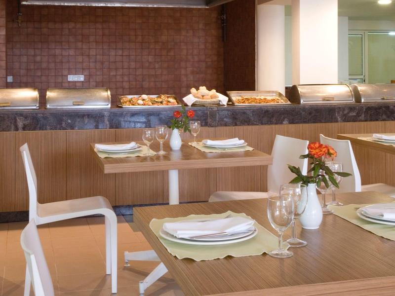 Modernes Esszimmer mit Holztischen, weißen Stühlen und Buffetbereich im Hintergrund.