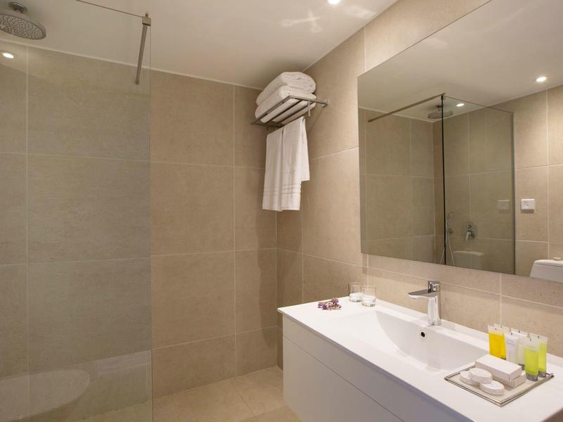 Modernes Badezimmer mit beiger Fliesenwand, Doppelwaschbecken, Spiegel und Klimagerät an der Wand.