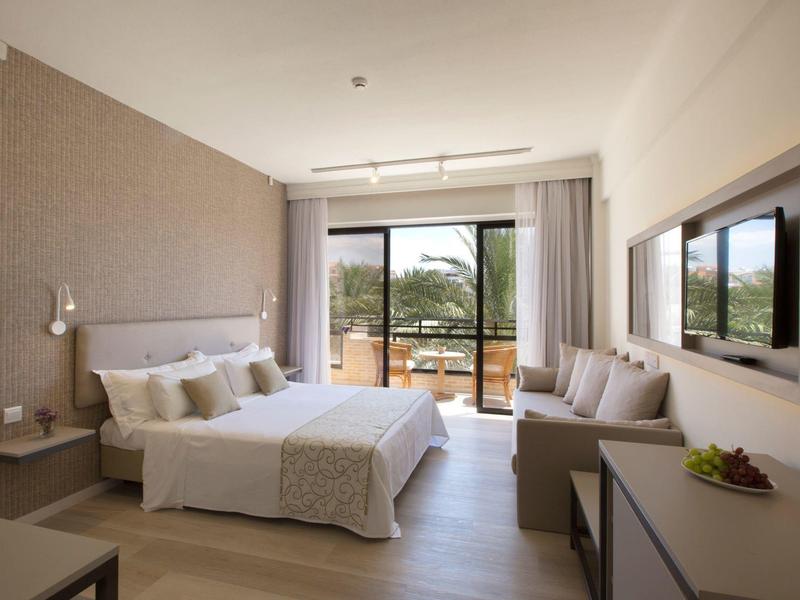 Helles, modernes Schlafzimmer mit großem Bett, Sofa, Balkon und neutralen Farben.