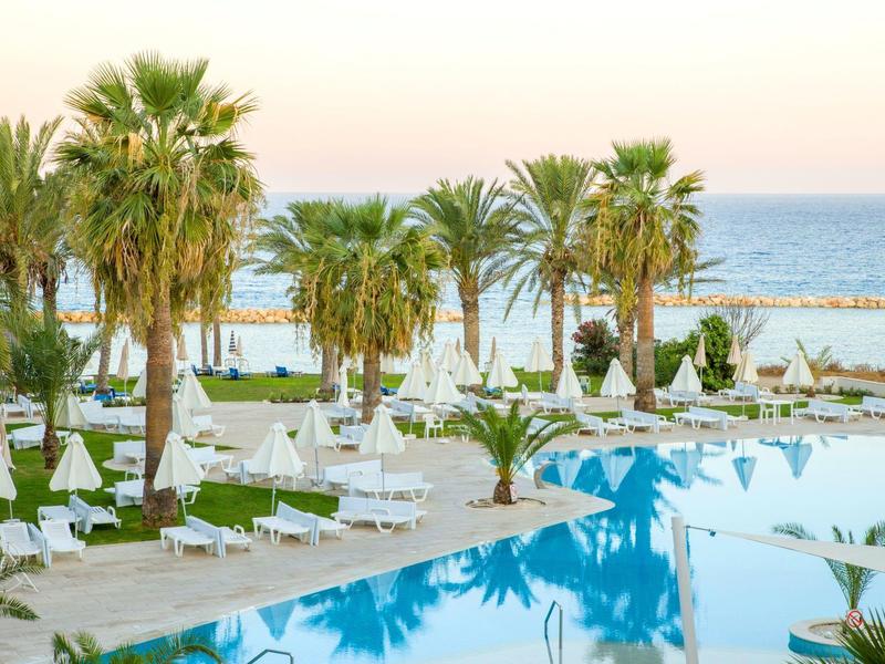 Hotelpool mit Liegestühlen und Palmen am Meer bei Sonnenuntergang.