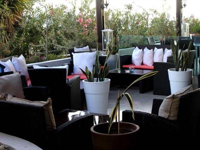 Gezellige buitenlounge met zwart meubilair en veel witte kussens omringd door groen.