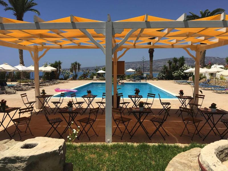 Kawiarnia na świeżym powietrzu z stolikami i krzesłami obok basenu pod żaglami przeciwsłonecznymi w słonecznym otoczeniu.