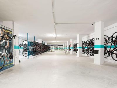 Großer, heller Fahrradkeller mit vielen an der Wand hängenden Fahrrädern und weißem Boden.