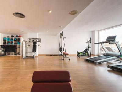 Heller Fitnessraum mit Holzboden, verschiedenen Trainingsgeräten und großen Fenstern.