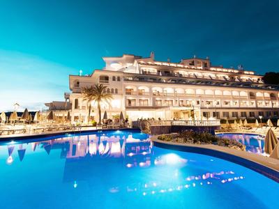 Un hôtel moderne avec une piscine éclairée la nuit et un ciel bleu clair.