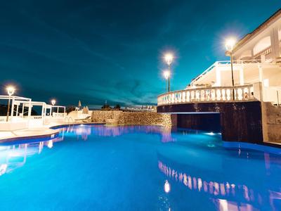 Piscine d'hôtel éclairée la nuit avec terrasse et coin salon.