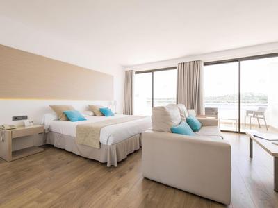 Chambre d'hôtel moderne avec lit double, canapé, sol en bois et grande fenêtre avec balcon.