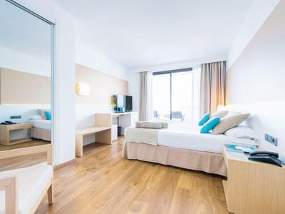 Helles Schlafzimmer mit Doppelbett, Holzboden, großem Spiegel und Fenster mit Blick nach draußen.