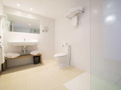 Salle de bain moderne et lumineuse avec lavabo, miroir, toilettes et douche.