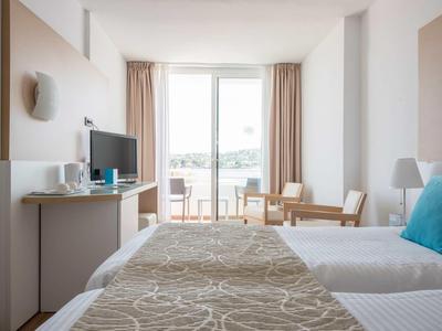 Chambre d'hôtel lumineuse avec lit double, bureau, télévision et balcon surplombant la ville.