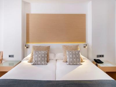 Modernes Hotelzimmer mit Doppelbett, zwei Zierkissen und Nachttischen auf beiden Seiten.