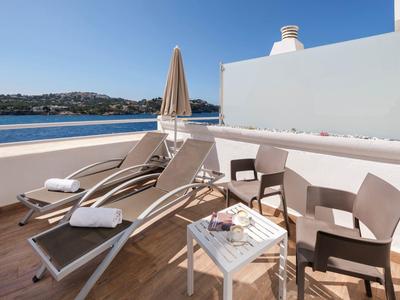 Balkon mit Liegestühlen, Tisch und zwei Stühlen mit Meerblick an einem sonnigen Tag.