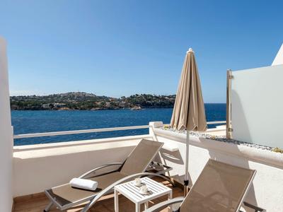 Zwei Liegestühle mit Handtüchern auf einer Terrasse mit Meerblick unter blauem Himmel.