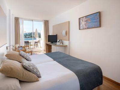 Helles Hotelzimmer mit zwei Betten, Balkon und Meerblick.