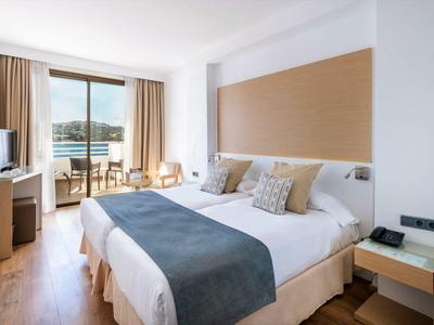 Modernes Hotelzimmer mit Doppelbett, Balkon und Meerblick bei Tageslicht.