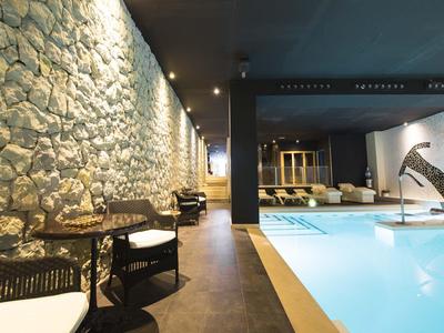 Espace piscine intérieure moderne avec mur en pierre, tables et chaises à l'hôtel.