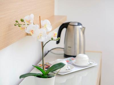 Weiße Orchidee auf einem Tisch neben einem Wasserkocher und einer Tasse in einem Hotelzimmer.