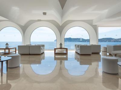 Espace lounge lumineux avec grandes arches et vue sur la mer par ciel clair.