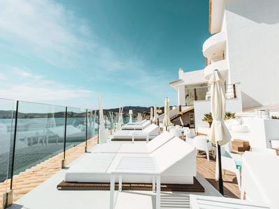 Chaises longues modernes sur une terrasse avec garde-corps en verre et vue sur la mer sous un ciel clair.