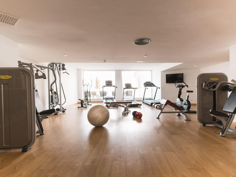 Salle de sport lumineuse avec sol en bois, divers appareils d'exercice et un ballon de gym.