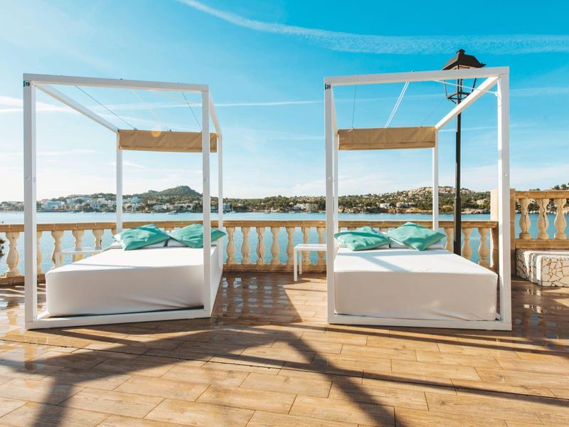 Deux lits de jour blancs avec des coussins turquoise sur une terrasse surplombant la mer.