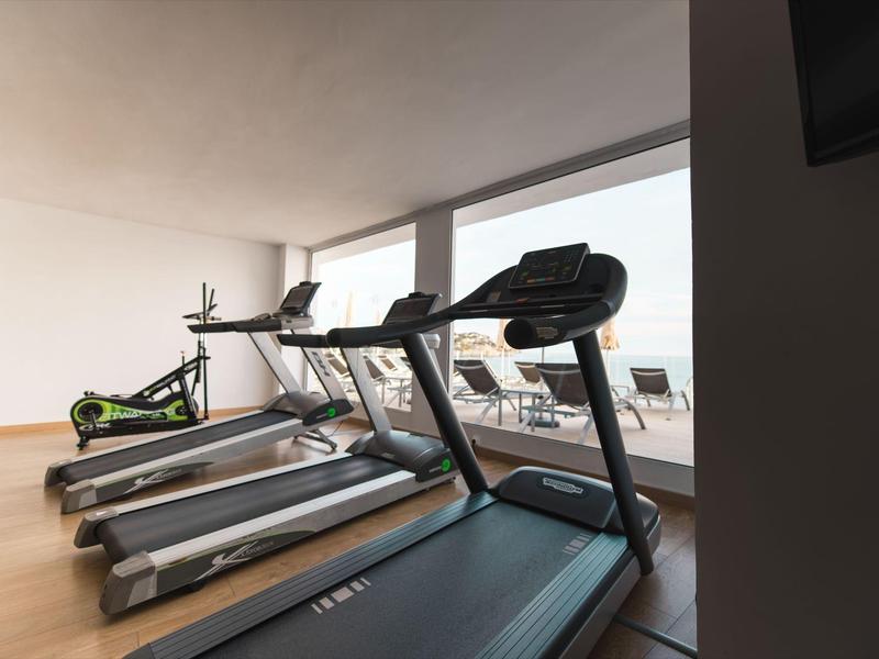 Équipements de fitness modernes dans une salle lumineuse avec grandes fenêtres et sol en bois.