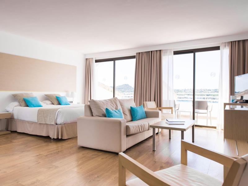 Chambre d'hôtel lumineuse avec deux lits, canapé et balcon avec vue.