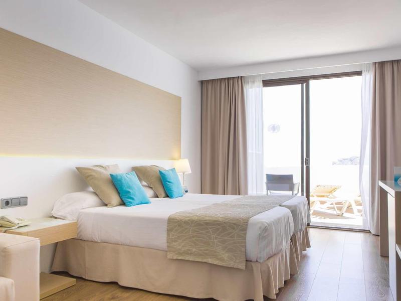 Chambre d'hôtel moderne avec lit double, balcon et rideaux clairs.