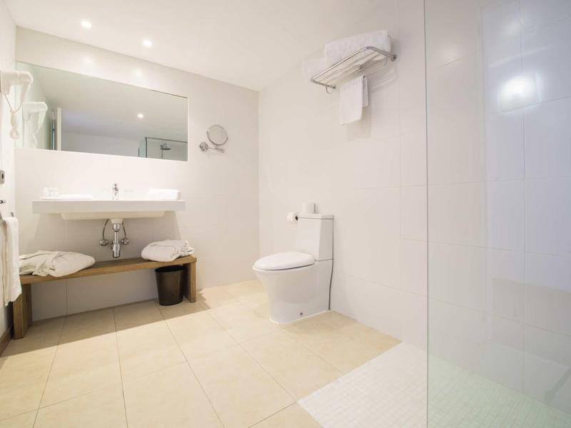 Salle de bain moderne et lumineuse avec lavabo, miroir, toilettes et douche.