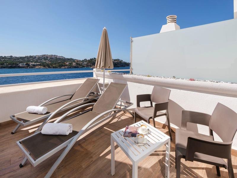 Balkon mit Liegestühlen, Tisch und zwei Stühlen mit Meerblick an einem sonnigen Tag.