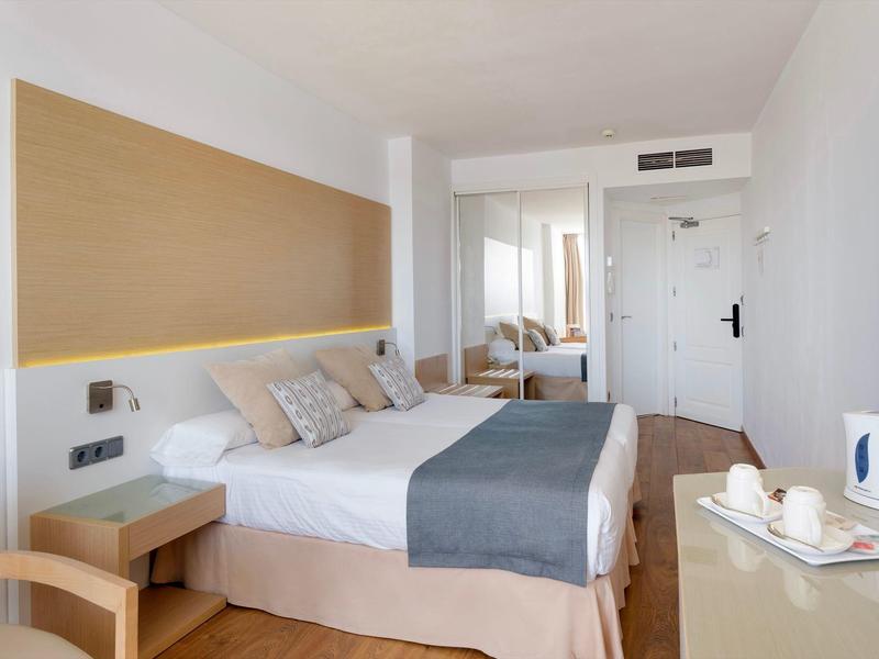 Modern eingerichtetes Hotelzimmer mit Doppelbett, Nachttischen und einem Schreibtisch mit Wasserkocher.