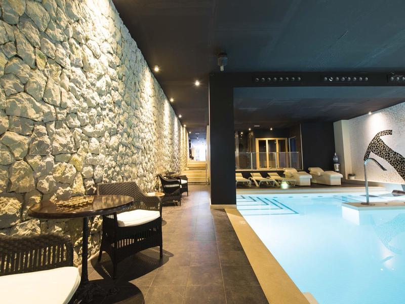 Espace piscine intérieure moderne avec mur en pierre, tables et chaises à l'hôtel.