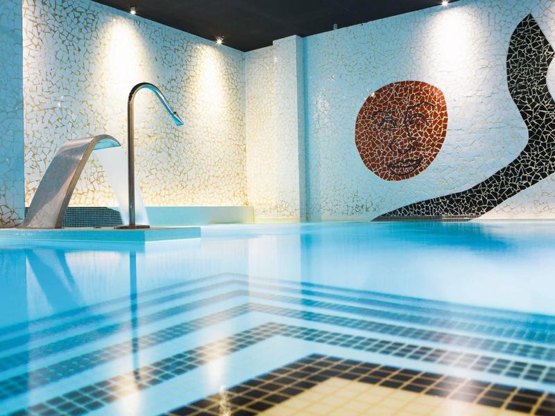 Piscine intérieure avec cascade et décoration murale en mosaïque dans un hôtel élégant