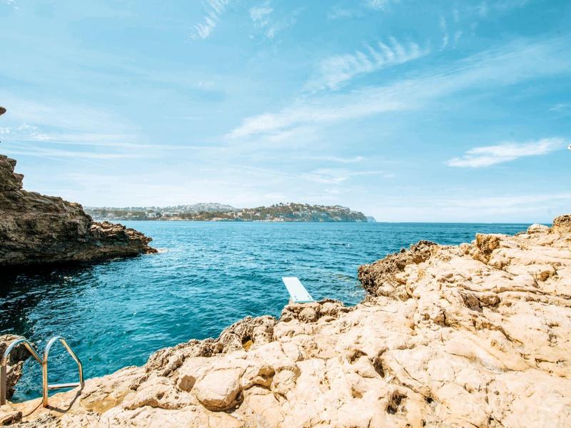 Côte rocheuse avec une échelle vers la mer sous un ciel bleu et vue dégagée.