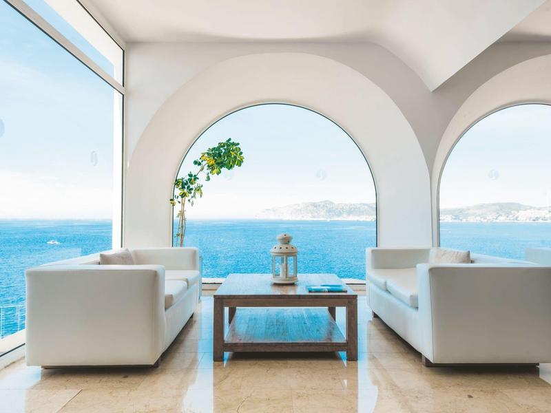Salon lumineux avec canapés blancs et vue sur la mer à travers de grandes arches.