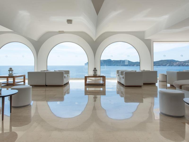Espace lounge lumineux avec grandes arches et vue sur la mer par ciel clair.