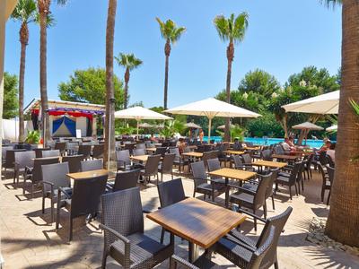 Outdoor-Bereich eines Hotels mit vielen Tischen, Stühlen und Sonnenschirmen neben dem Pool.