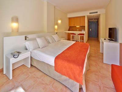 Camera d'hotel accogliente con letto grande, copriletto arancione e angolo cottura piccolo.