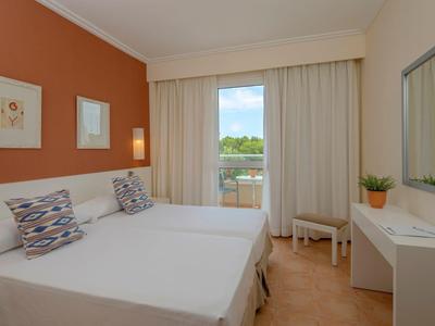 Camera d'hotel moderna con letto matrimoniale, parete arancione e balcone con vista sul verde.