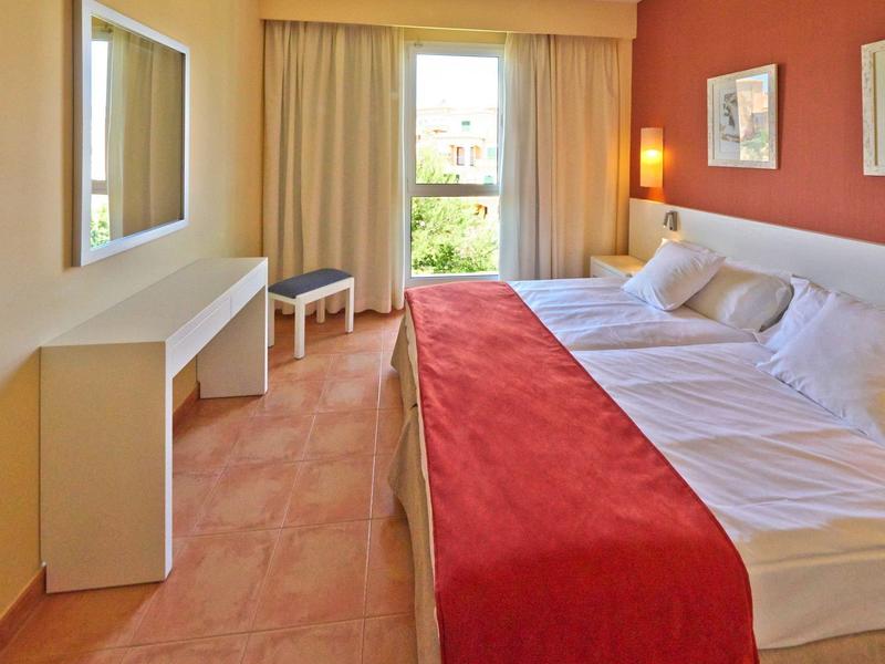 Camera d'hotel luminosa con letto matrimoniale, biancheria bianca, coperta rossa e finestra con tende.