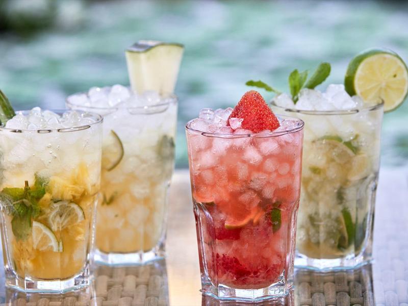 Quattro bevande rinfrescanti con ghiaccio e frutta su un tavolo all'aperto.