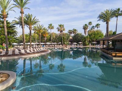Grand espace piscine avec des palmiers et des chaises longues sous un ciel bleu.