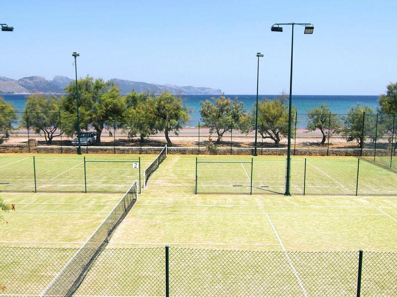Terrain de tennis vert avec des arbres et vue sur la mer en arrière-plan.