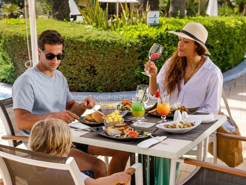 Une famille profite d'un repas en plein air avec boissons et soleil en vacances.