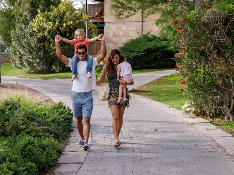 Famille avec un enfant porté sur les épaules marchant sur un trottoir dans un quartier verdoyant.