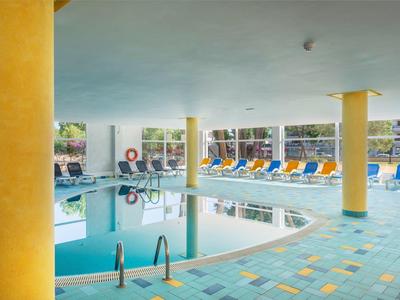 Piscina interna con pilastri gialli e sedie a sdraio blu intorno.